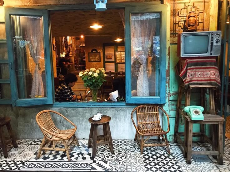 3 Cách Chọn Nội Thất Quán Cà Phê – Giải Pháp Tối Ưu Không Gian 4 Nội thất quán cà phê phong cách retro với đồ trang trí cổ điển, bàn ghế mây tre và cửa sổ màu xanh nổi bật.
