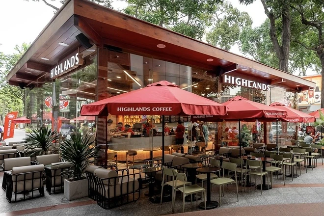 Thiết Kế Quán Cafe Highlands Bản Sắc Việt Trong Không Gian Hiện Đại 6 Khu vực ngoài trời Highlands Coffee với bàn ghế gỗ, ô che nắng màu đỏ và cửa kính lớn.